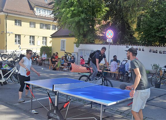 Buntes Treiben Tischtennispartie und Menschen im Hintergrund, die am Straßenrand sitzen.
