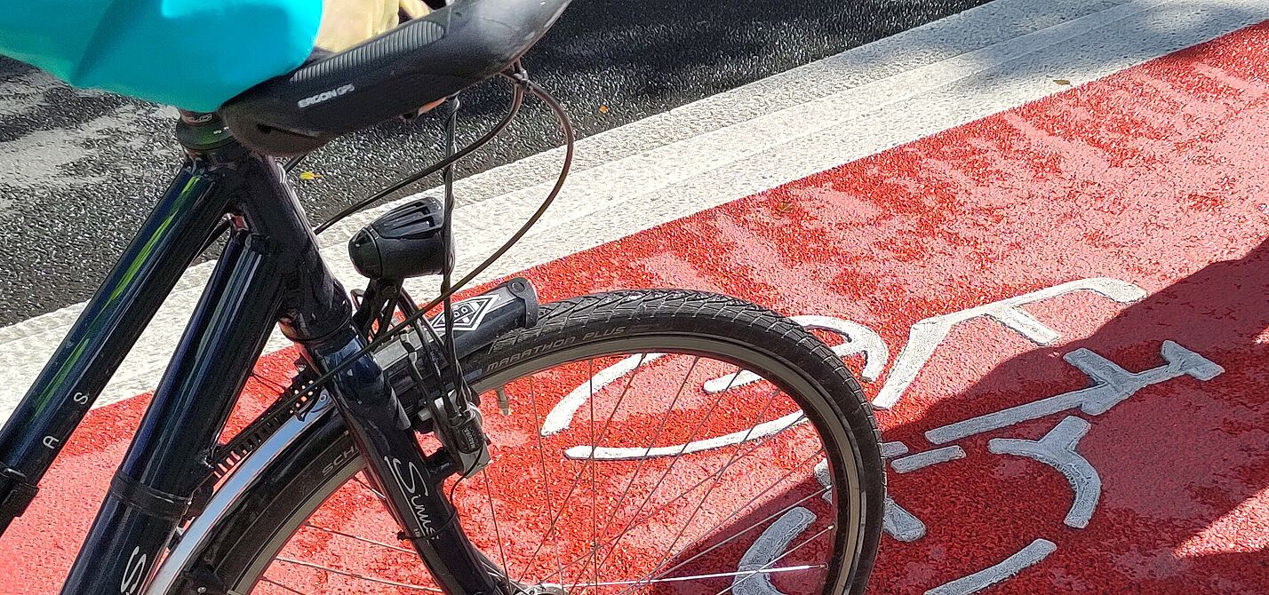 Neu markierter Radfahrstreifen mit flächiger Roteinfärbung. Man sieht auch einen Fahrradlenker.